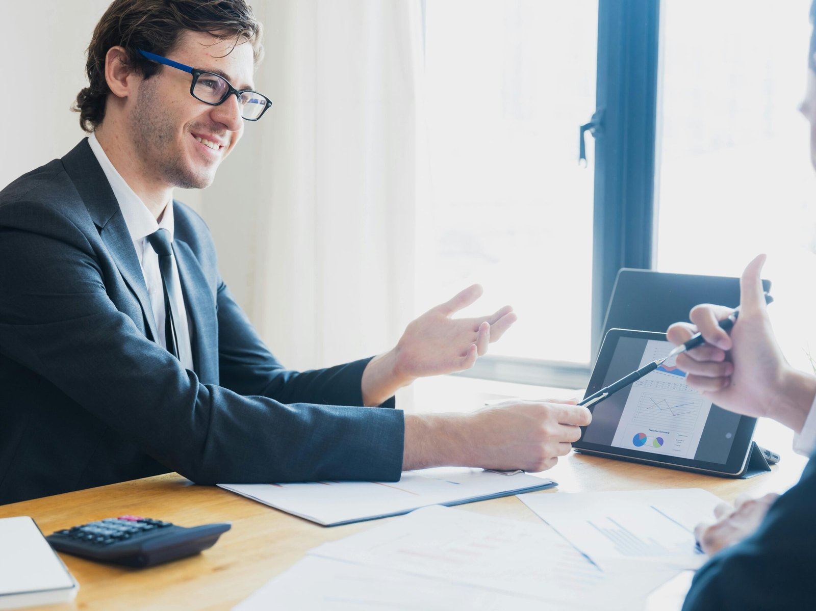 Two businessmen in formal attire discussing a business report in an office setting with a tablet.